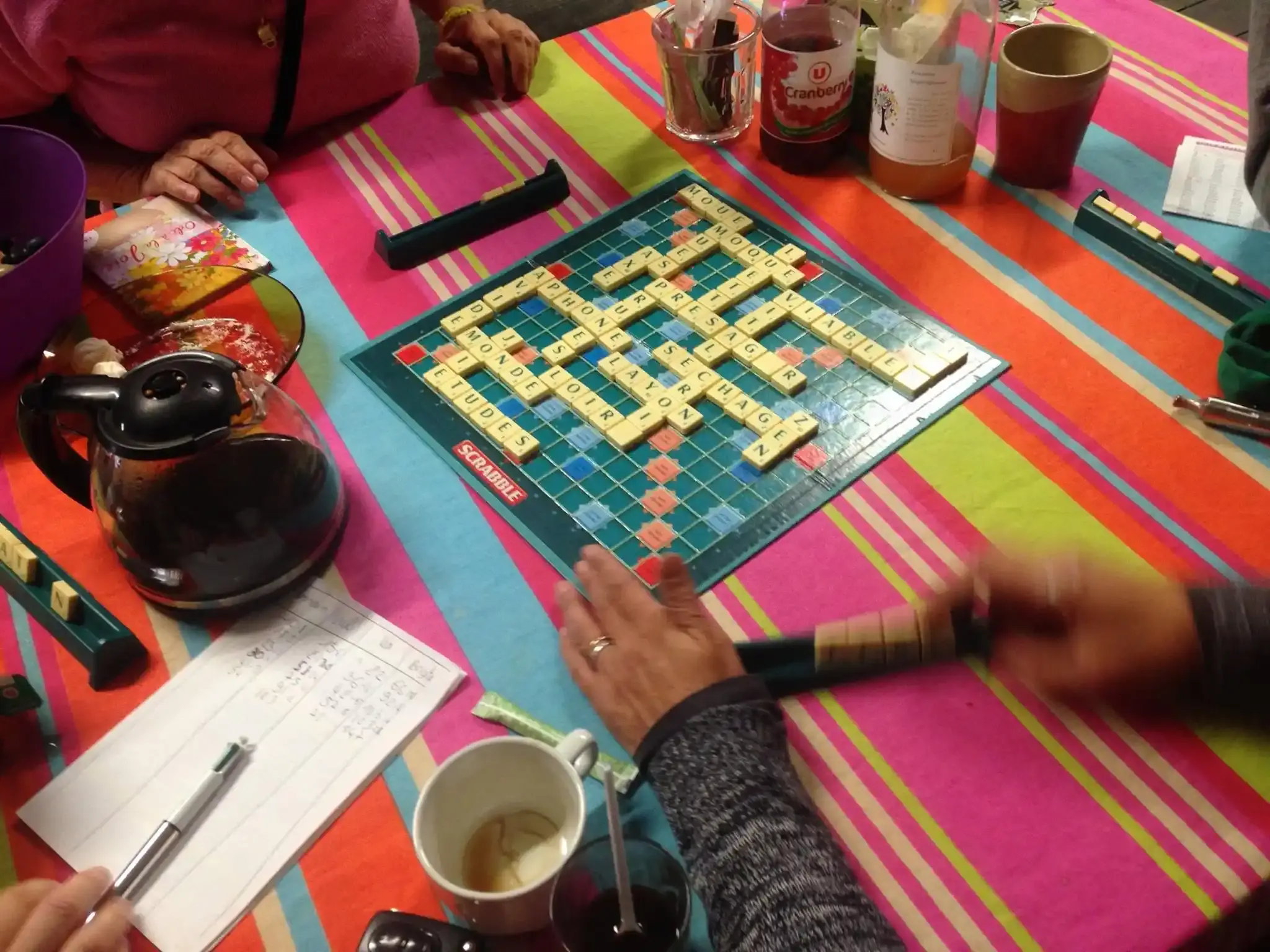 Une partie de Scrabble sur une nappe colorée, entourée de tasses et d’une théière