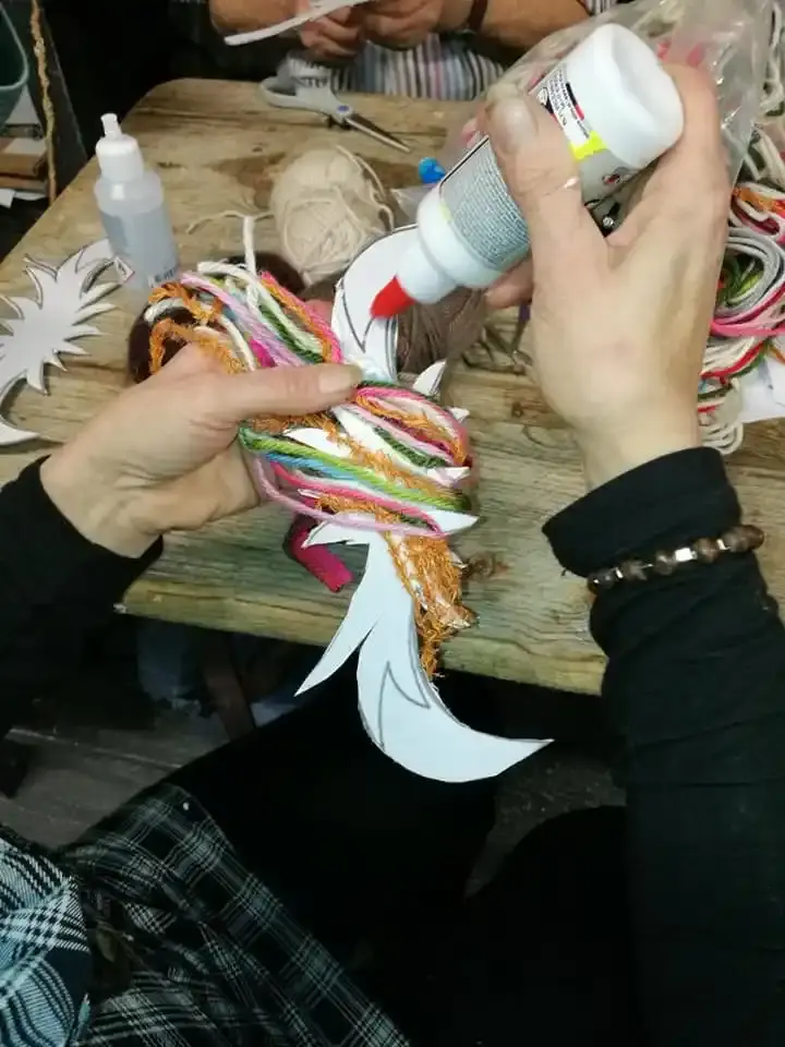 Des mains collent des fils de laine multicolores sur des oiseaux en papier