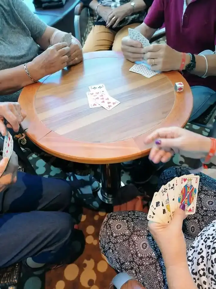 Des mains tiennent des cartes à jouer autour d’une table en bois