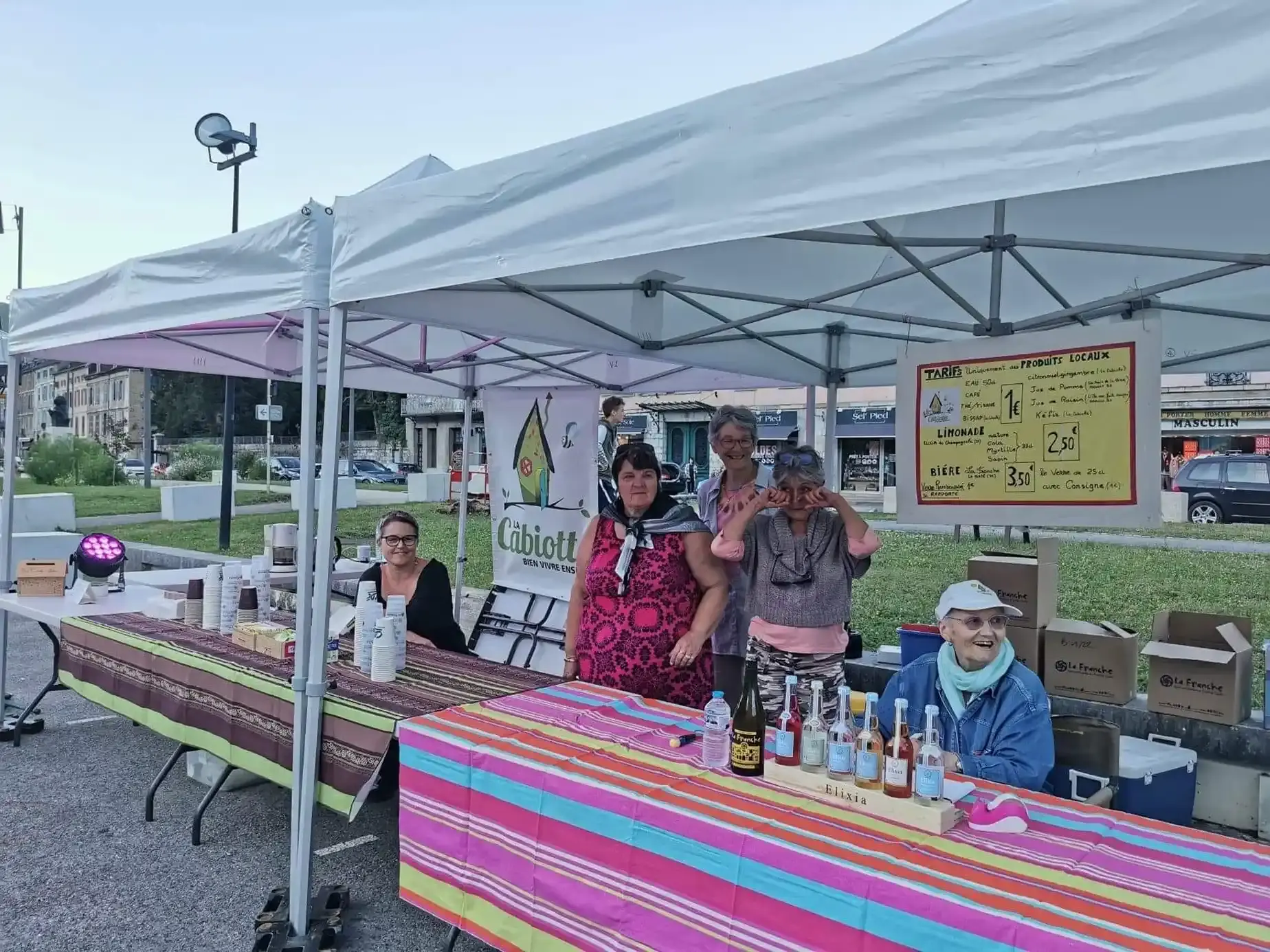 Quatre bénévoles souriantes derrière le stand de La Cabiotte sur un marché