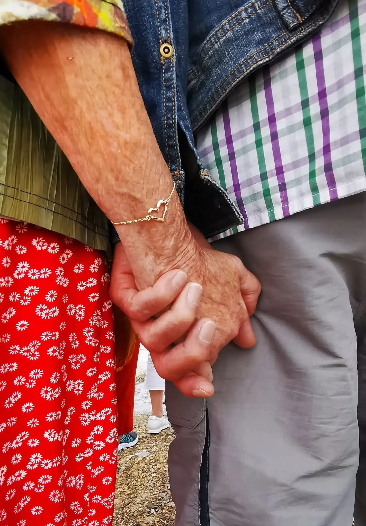 Deux mains âgées qui se tiennent, l’une portant un bracelet en forme de cœur